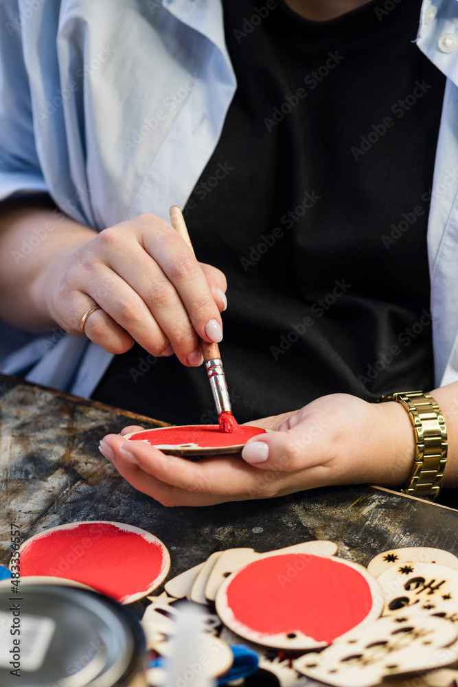 Obraz premium Process making handmade wooden Christmas toys in carpentry woodworking workshop. Hands of master paint round wooden surface red. Handmade. Small business concept.