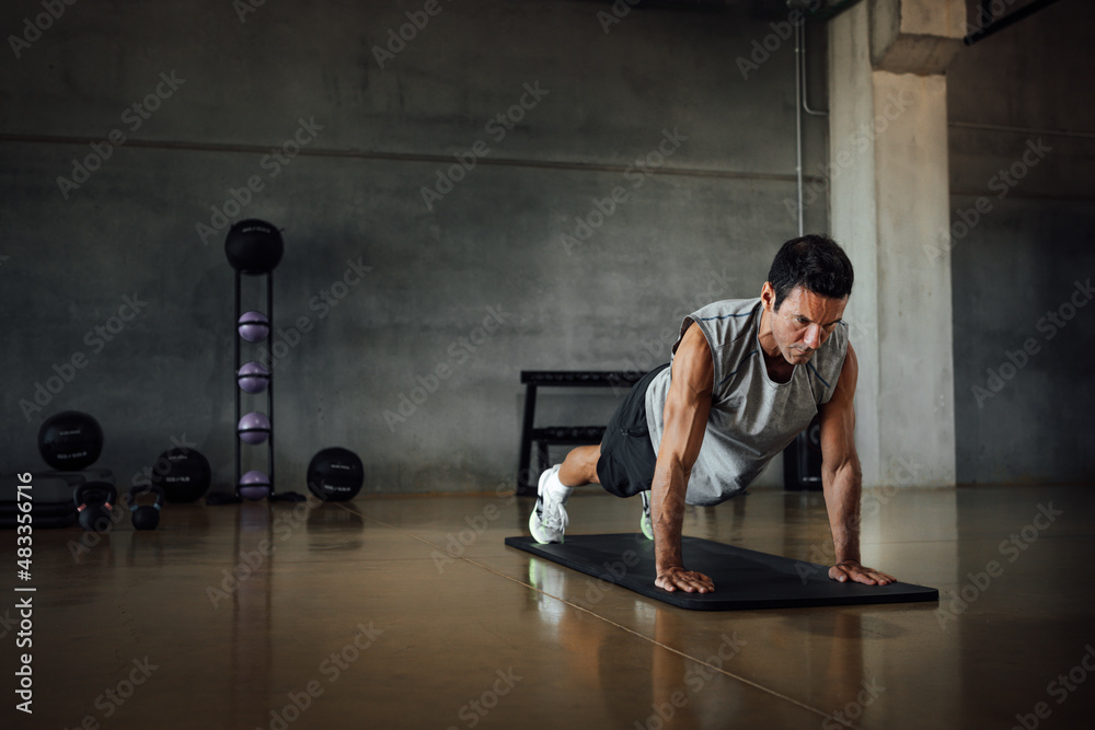 Athletic man doing pushups exercise at dark gym.
