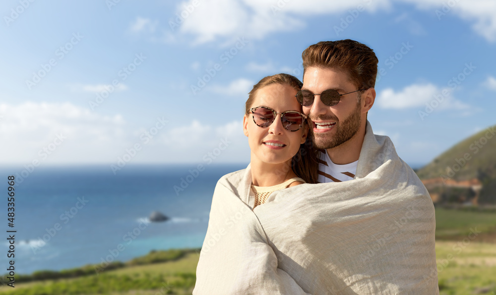 love, travel and tourism concept - happy couple in sunglasses covered with blanket hugging over big sur coast of california background love, travel and tourism concept - happy couple in sunglasses covered with blanket hugging over big sur coast of california background