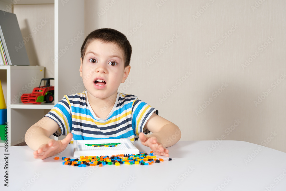 A boy of 4 years old plays with a mosaic, collects a picture from small plastic parts. Development of fine motor skills in children A boy of 4 years old plays with a mosaic, collects a picture from small plastic parts. Development of fine motor skills in children