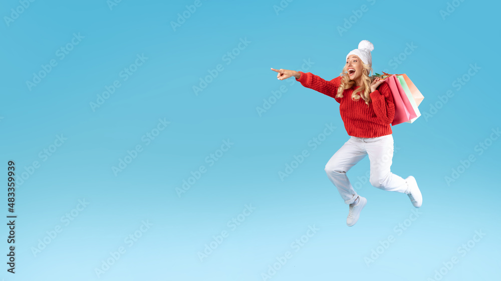 Excited blonde woman jumping with shopping bags at studio