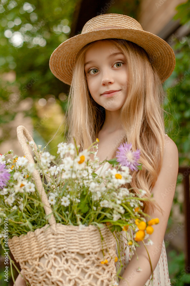 Cute preteen girl in straw hat with basket of wildflowers in green country garden