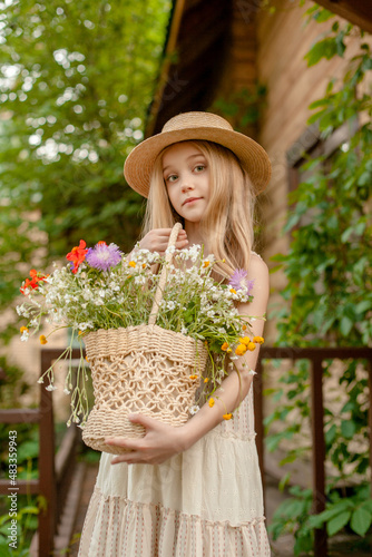 Dreamy preteen girl with basket of wildflowers standing in courtyard of rural house