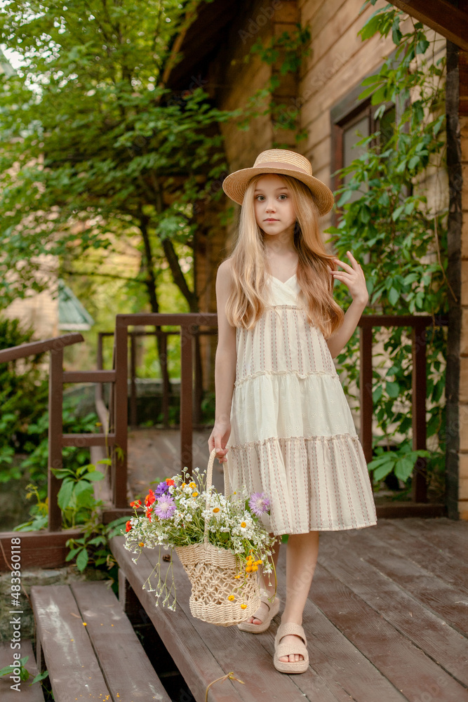 Obraz premium Carefree tween girl with basket of wildflowers standing on doorstep of country house