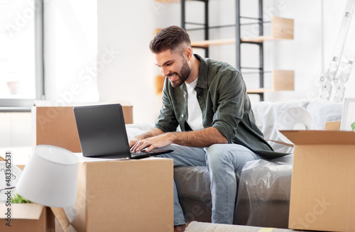 moving, people and real estate concept - happy smiling man with laptop computer at new home