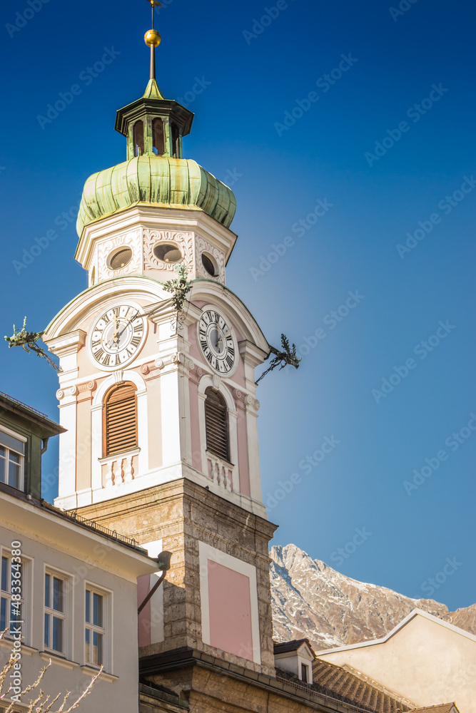 Tower clock on city hall in Innsbruck, Austria. Innsbruck landmark on sunny day in winter. Ancient church and Alps mountains on background, Innsbruck. Historical architecture in Tyrol, Austria.