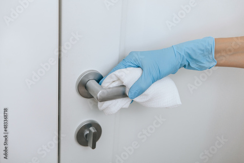 Cleaning black door handles with an antiseptic wet wipe and blue gloves. Sanitize surfaces prevention in hospital and public spaces against corona virus. Woman hand using towel for cleaning.