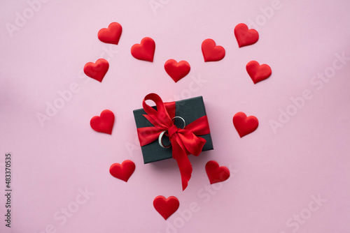 A jewerly box with a red ribbon and two engagement rings surronded by a heart shape