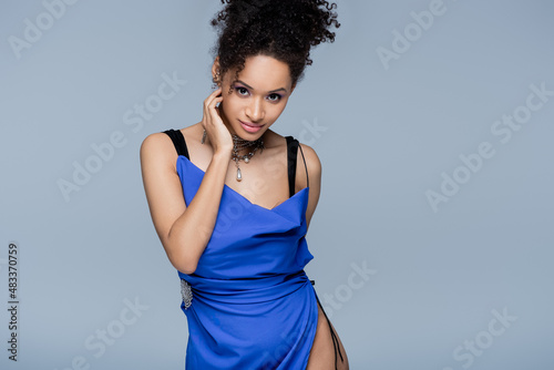 african american model in bright blue dress looking at camera while posing isolated on grey.