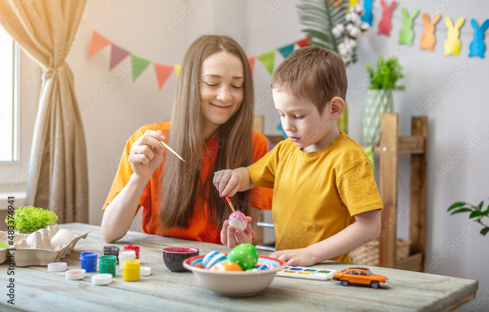 Fototapeta premium Mom and little child together are coloring eggs and having fun. Concept of family preparation for Easter, festive spring mood
