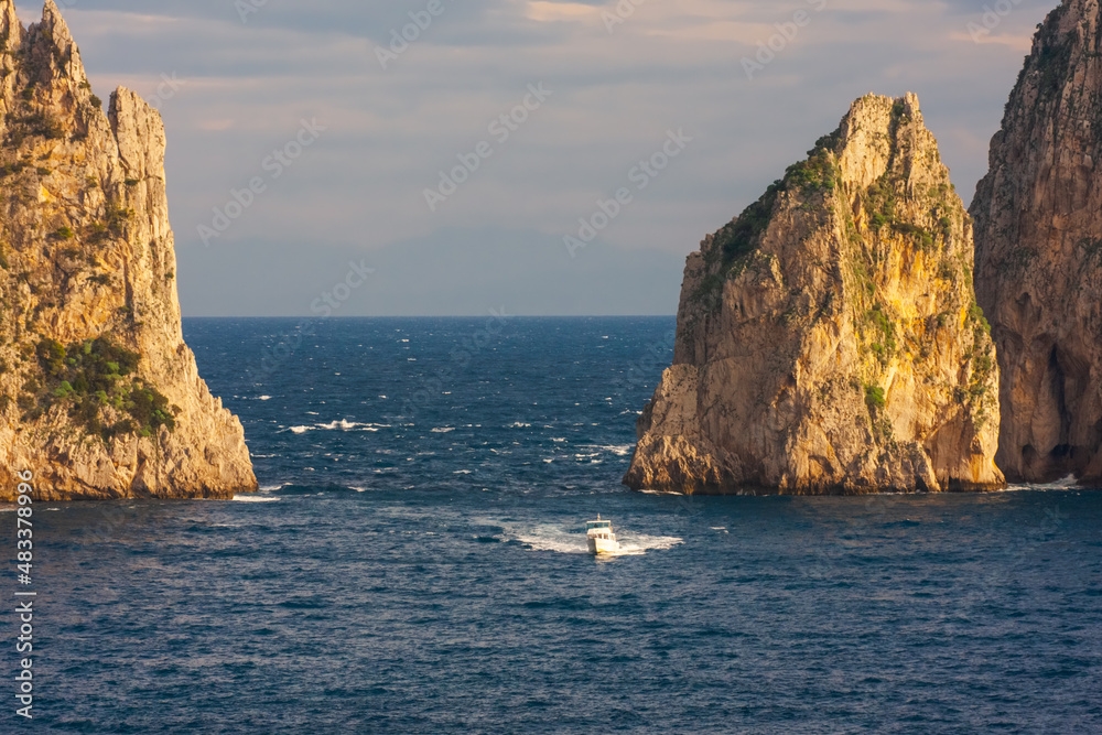 Small tourist boat sailing between Faraglioni (huge rocky stacks), Capri, Italy Small tourist boat sailing between Faraglioni (huge rocky stacks), Capri, Italy