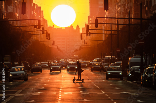 Valencia port avenue, giant sun during sunset, silhouette of man on electric scooter and cars