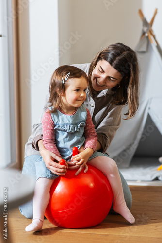 family, leisure and people concept - happy mother playing with little baby daughter bouncing on hopper ball at home photo