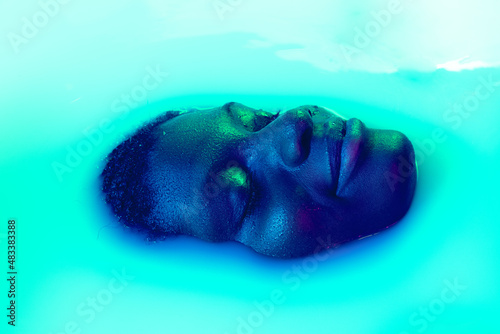 Close up female face of african girl in milk bath with soft white glowi in neon light. Modern neoned colors  foam. Beauty  fashion  style  skincare concept.