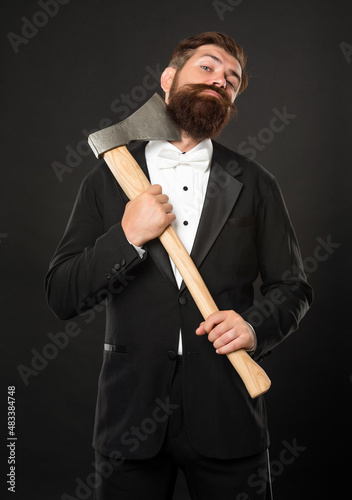 Bearded man scraping chin with axe dark background, barbering