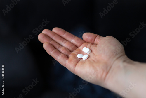 Close-up of a caucasian man holding three white medicine or vitamin pills in palm of hand.