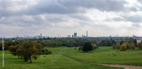 Beautiful green meadow in park with modern city skyline against cloudy sky, London skyline seen from primrose hill photo