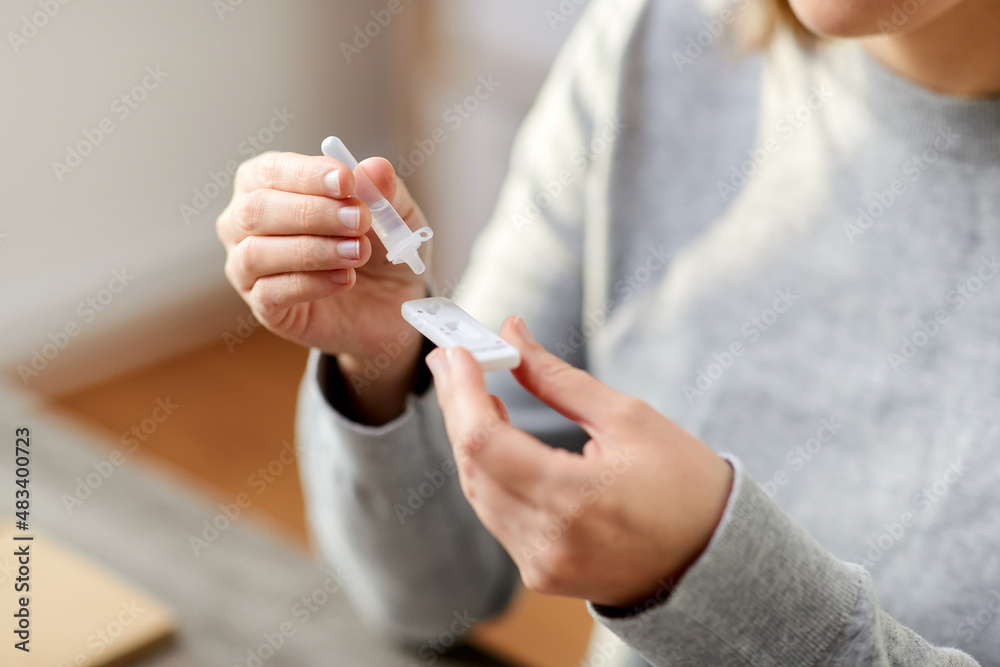 Obraz premium medicine, self testing and pandemic concept - close up of woman making coronavirus test and dropping reagent to cartridge at home