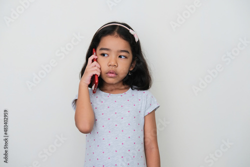 Asian kid showing confused expression when answering a phone call photo
