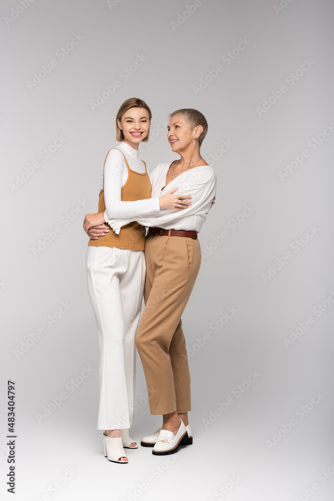 full length of pleased middle aged mother and young daughter hugging on grey full length of pleased middle aged mother and young daughter hugging on grey