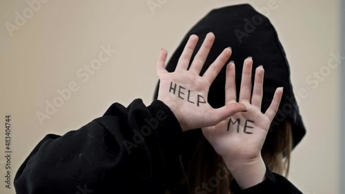 Teenage girl, covering her face with a hood, shows her palms with the inscription HELP ME. photo