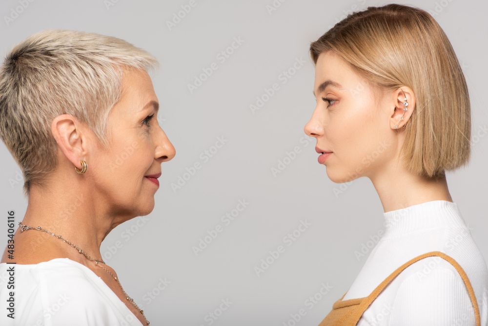 side view of young daughter and mature mother looking at each other isolated on grey side view of young daughter and mature mother looking at each other isolated on grey