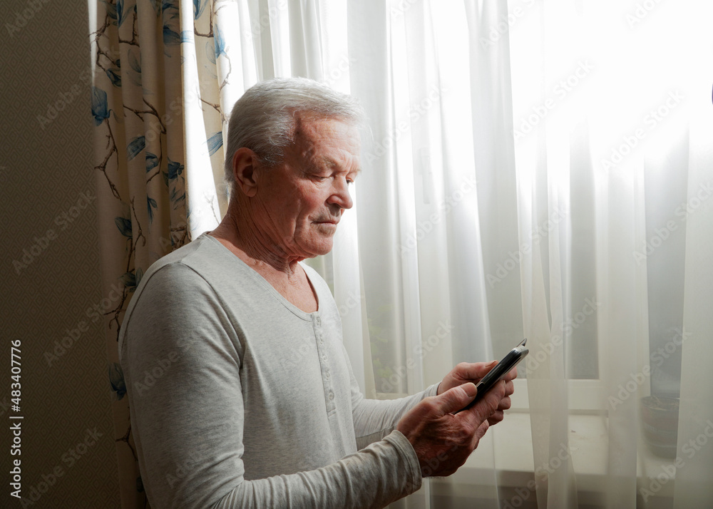 Retired male chatting with friends in social media, typing on smartphone. Happy senior man using phone at home. Retired male chatting with friends in social media, typing on smartphone. Happy senior man using phone at home.