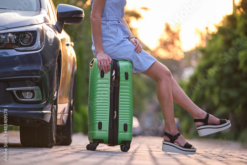 Murais de parede Closeup of young woman slim legs resting on suitcase bag beside car