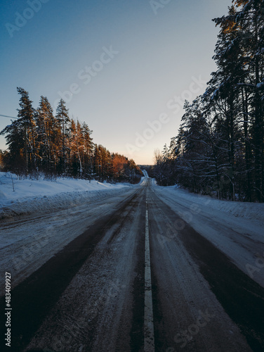 Country snowy road through coniferous forest in winter. Sunset