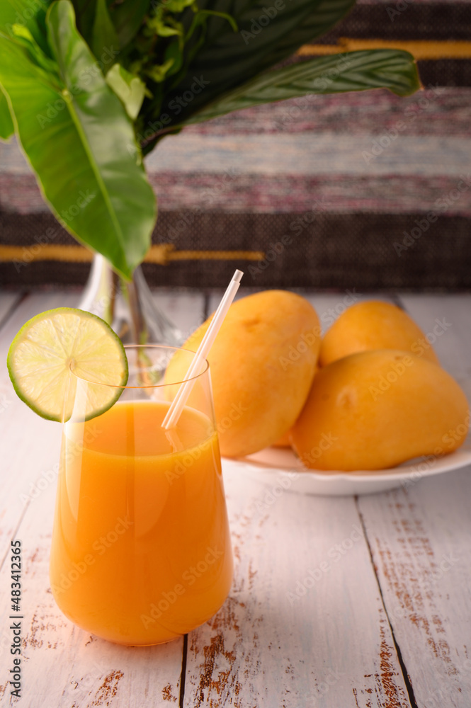 Fototapeta premium Mango mocktail and plate of mango. Vase with tropical leaves on left