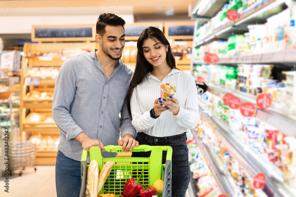 Middle Eastern Spouses Holding Dairy Products Doing Grocery Shopping In Supermarket