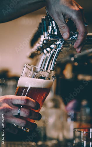 Canvas Print bartender hand at beer tap pouring a draught beer in glass serving in a bar or p
