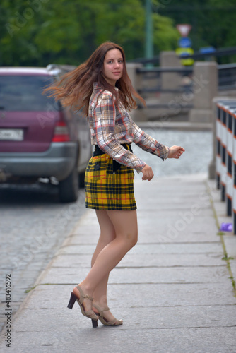pretty brunette girl in a plaid blouse and skirt on a city street