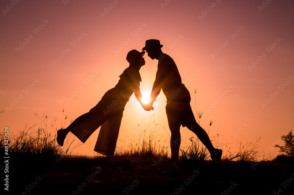 Silhouette of a couple in romantic acting on meadow, sun flare background
