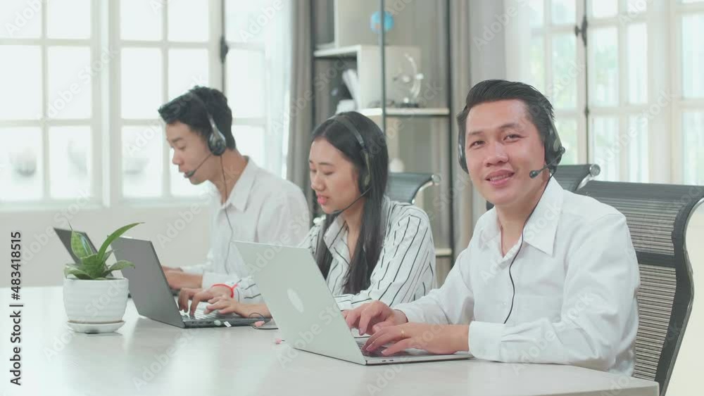 A Man Of Three Asian Call Center Agents Wearing Headset Smiling To Camera While Two Of His Colleagues Speaking And Typing During The Call With Customer At The Office
A Man Of Three Asian Call Center Agents Wearing Headset Smiling To Camera While Two Of His Colleagues Speaking And Typing During The Call With Customer At The Office