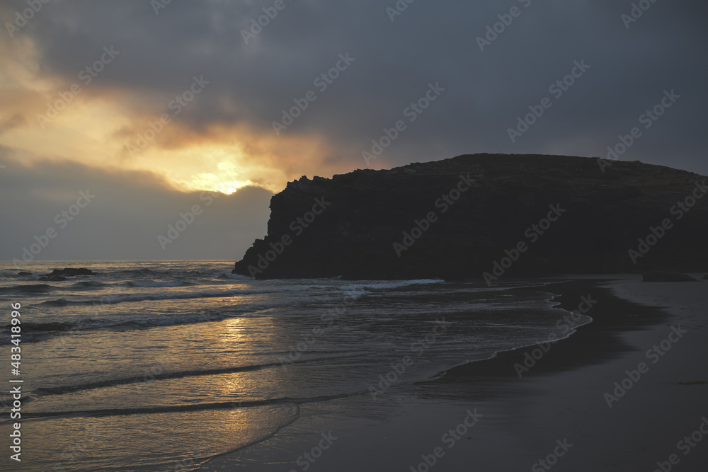 sunset on the beach with a rock in the landscape