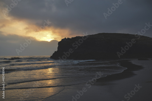 sunset on the beach with a rock in the landscape