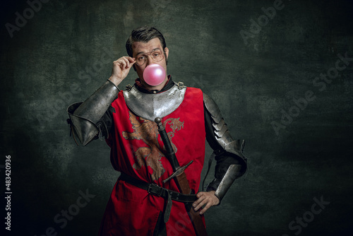 Foto Comic portrait of funny medieval warrior or knight with dirty wounded face holding sword isolated over dark background
