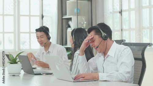 A Man Of Three Asian Call Center Agents Wearing Headset Is Tired Because Two Of His Colleagues Are Talking During Working At The Office
 photo