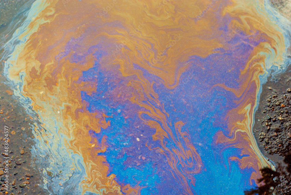 Oil stains on wet asphalt. Puddles are contaminated with multicolored streams of oil. The concept of environmental pollution, oil spills and environmental problems.
