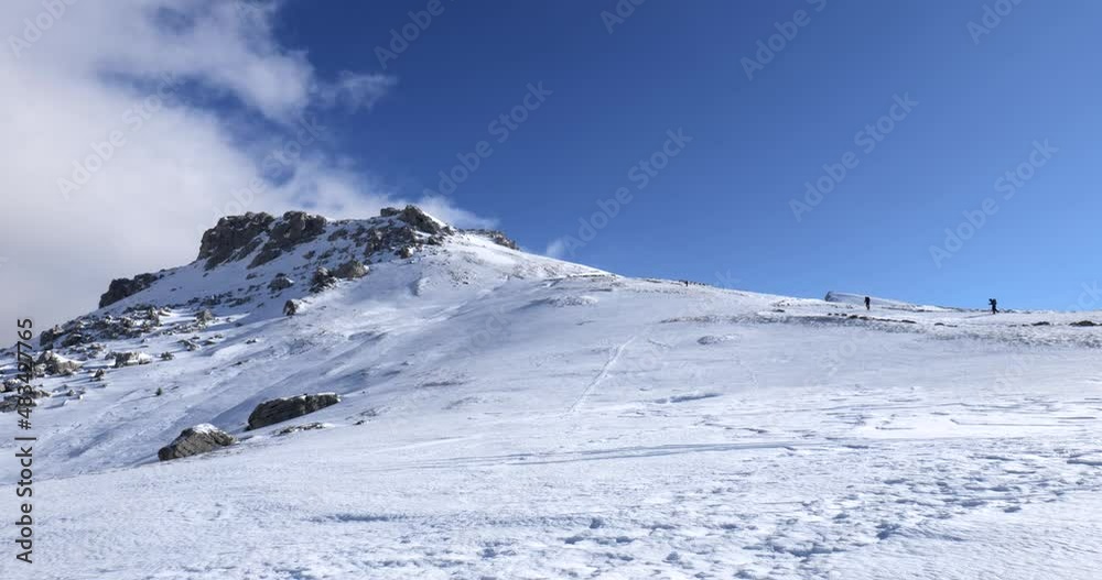 Mountaineers walking, hiking on a winter sunny day to reach the mountain peak. Wind and clouds are passing in the sky. Traveling and connecting with nature. 

