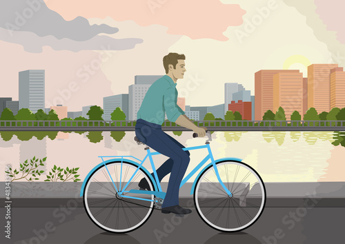 Fototapeta Naklejka Na Ścianę i Meble -  A man is riding along the embankment on a blue bicycle and wearing a blue shirt and trousers. Sports and people. The guy on the bike. A cyclist. To work by bike. Rest and health. 