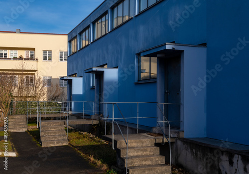 Block of flats with blue facade, small stairs at the entrances in Stuttgart Germany on a blue sky day. Linear geometrical architecture from the modern movement era.