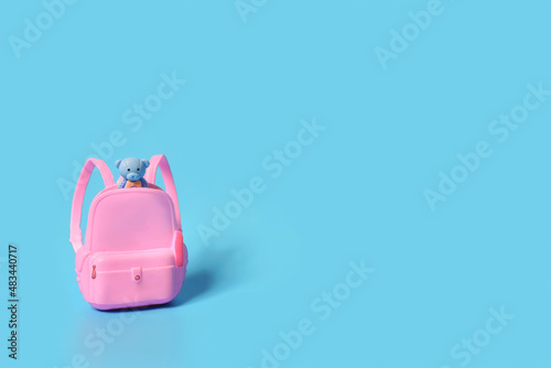 Pastel pink school bag with 
 blue bear inside against a blue background. Surreal modern trawel concept. Back to school minimal concept. photo