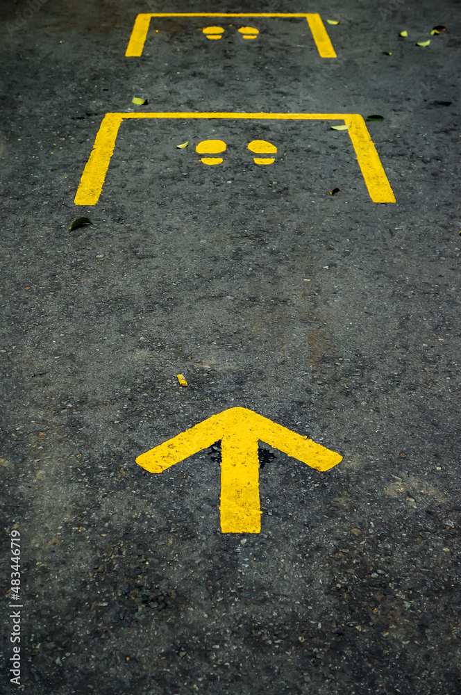 Yellow arrow and footsteps street guide sign on black asphalt. Guidance and regulation of social distancing during a global pandemic.