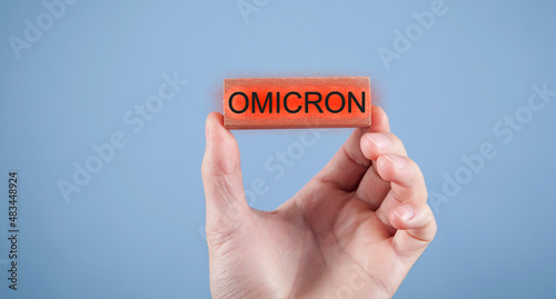 Male hand showing Omicron text on wooden block.