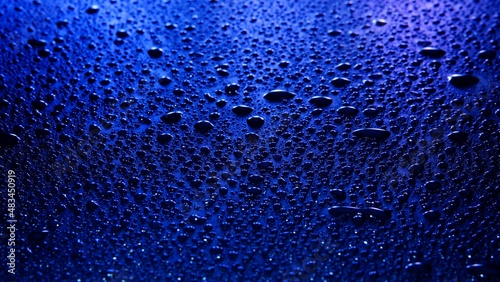 Many drops of water on a blue surface in the dark background, selective focus
