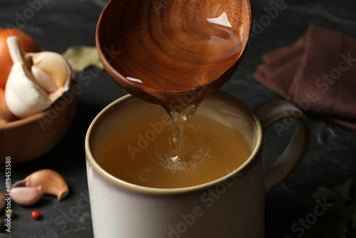 Pouring hot delicious bouillon into cup on black table, closeup