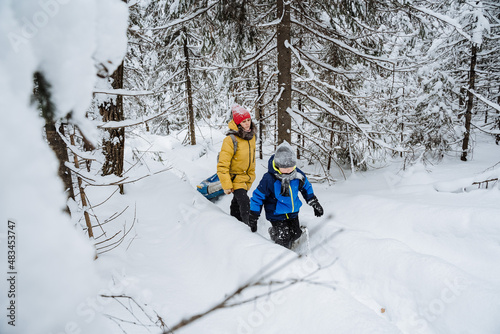 A child with his mother walks along the road in the winter forest. A warmly dressed family walks through the snowdrifts. A boy hike with his parent in the mountains in a cold climate.