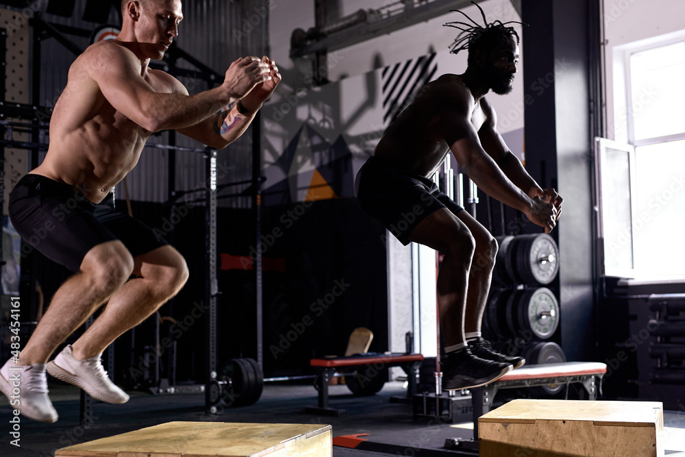 Young strong fit sweaty muscular men with big muscles doing box jump  workout in modern cross fit gym, training together, real people exercise.  Handsome two shirtless guys are engaged in sport foto